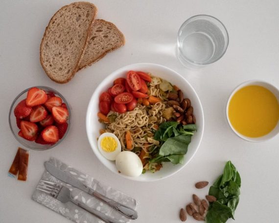 A balanced meal featuring a variety of healthy ingredients including noodles, eggs, almonds, strawberries, and fresh vegetables.