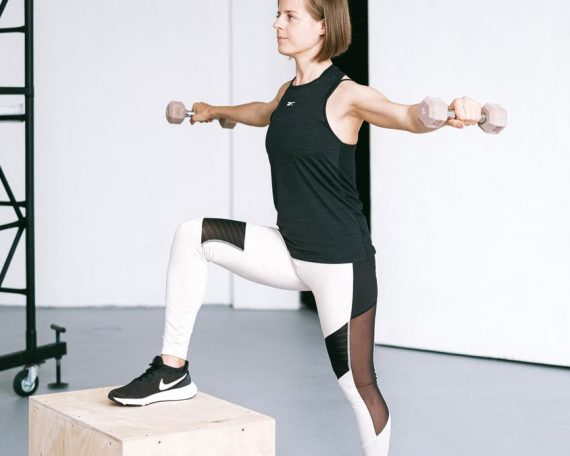 Woman performing fitness exercise with dumbbells in a gym setting, showcasing strength and balance.